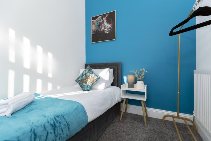 Modern bedroom with single bed, turquoise bedding, blue accent wall and white bedside table