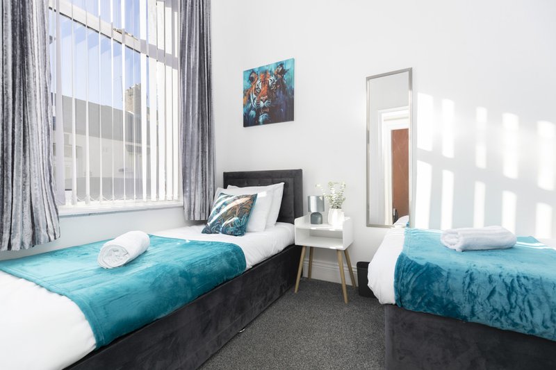 Modern twin bedroom with two beds, turquoise bedding, white pillows, and bright window light