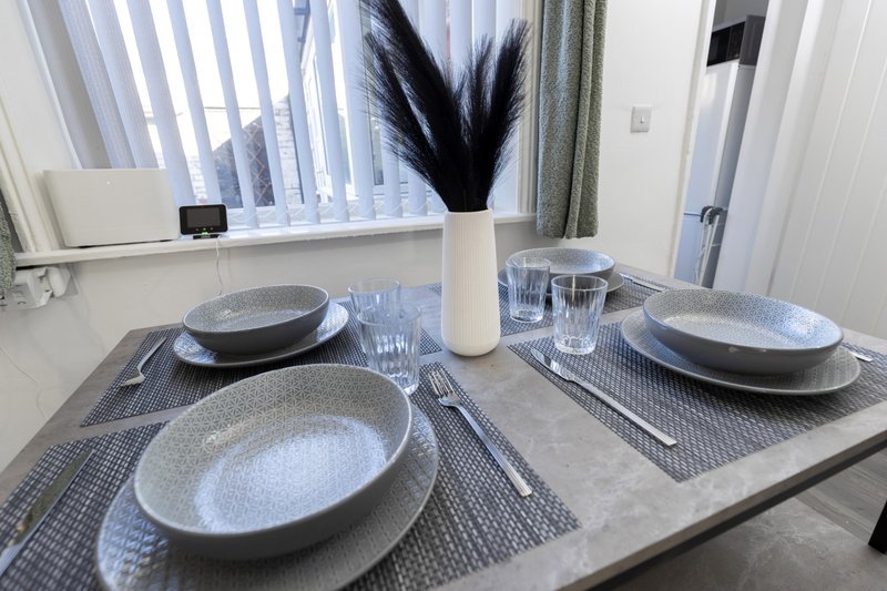 Dining table set for four with plates, glasses, cutlery and black feather vase