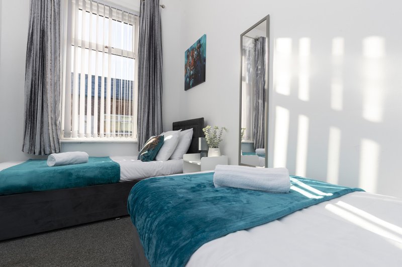 Bright bedroom with two single beds, teal bedding, grey curtains and window light