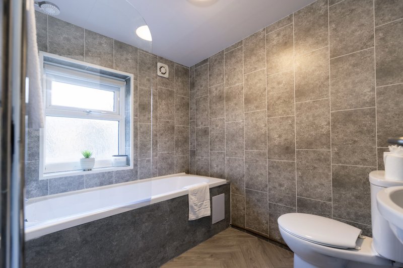 Modern bathroom with tiled walls, bathtub, toilet, and window with natural light