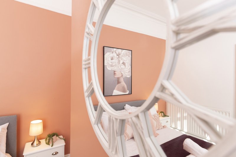 Bedroom with peach walls, white round mirror, bedside lamp and framed artwork