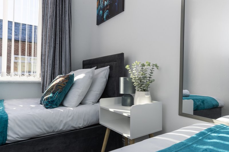 Modern bedroom with black bed frame, white bedding, grey curtains and potted plant on nightstand