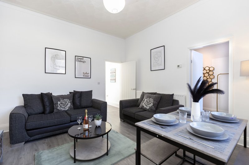 Open-plan living and dining area with dark sofa, round coffee table, dining table with place settings