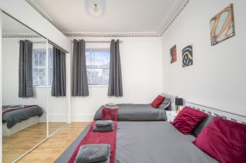 Bright bedroom with two beds, red and grey bedding, mirror, wooden floor and wall art