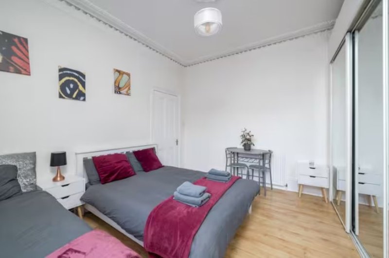 Bedroom with double bed, grey bedding, red pillows, wooden floor and wall art