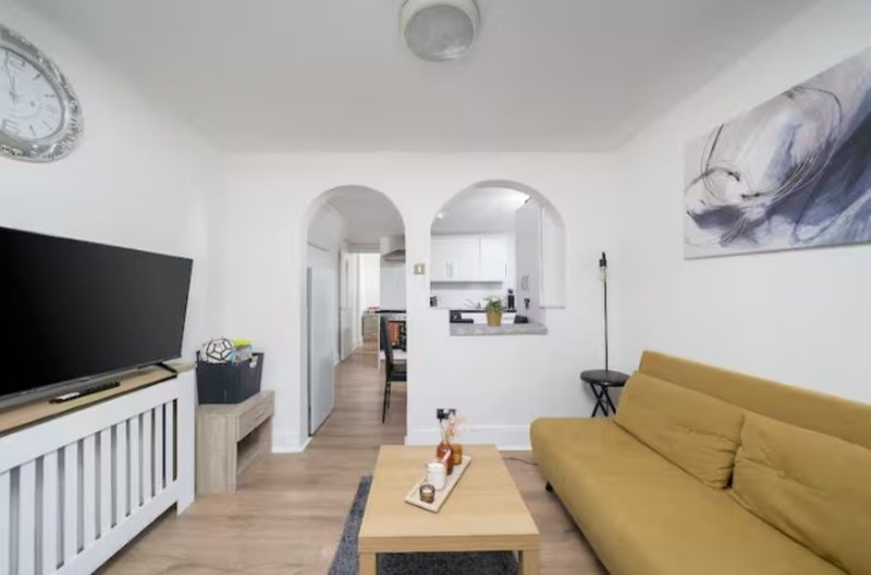 Open-plan living room with yellow sofa, wooden coffee table, TV and kitchen beyond