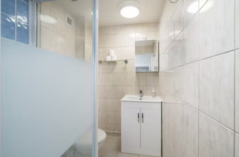 Clean modern bathroom with white vanity, tiled walls, mirror and frosted shower enclosure