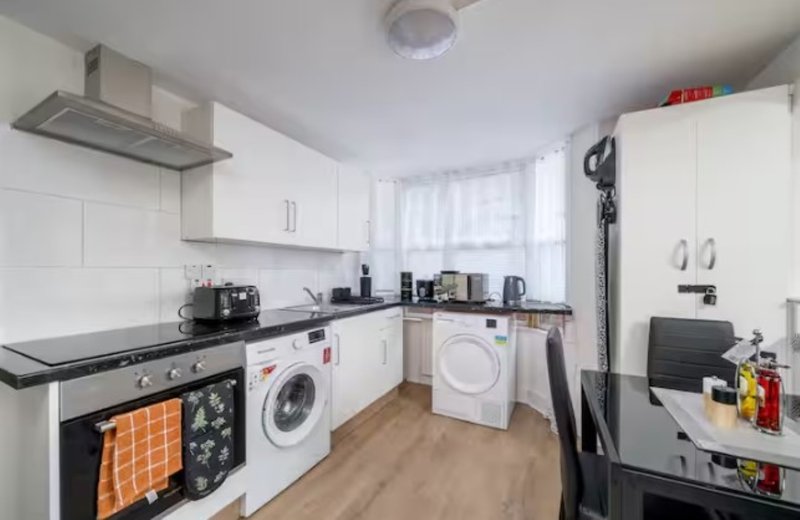 Modern kitchen with white cabinetry, black countertops, integrated appliances and washing machine