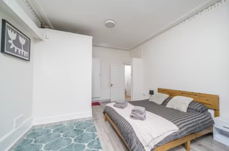 Bedroom with wooden bed frame, striped bedding, white walls and light wooden flooring