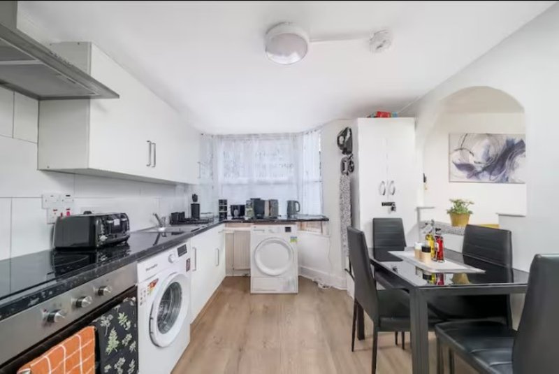 Open-plan kitchen and dining area with white cabinetry, gas range, washing machine and dining table