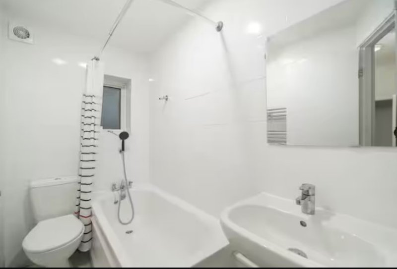 Clean modern bathroom with white tiled walls, bathtub, toilet, sink and mirror