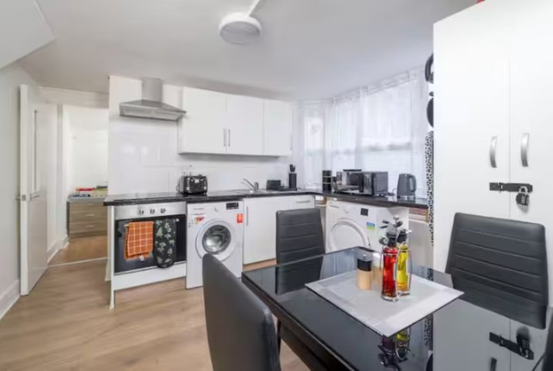 Modern kitchen with white cabinetry, black countertops, integrated appliances and dining table