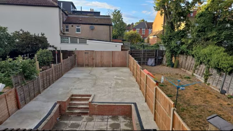 Rear garden with paved patio, wooden fencing, brick raised beds and surrounding properties visible