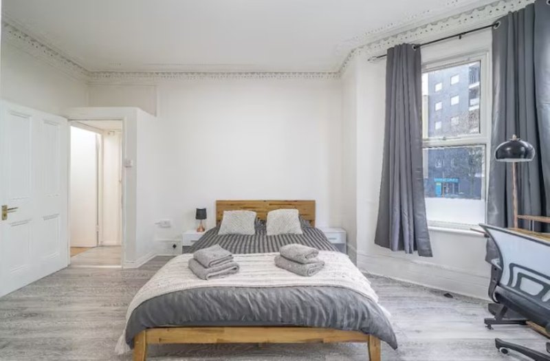 Bright bedroom with wooden bed frame, grey bedding, window with curtains and desk area