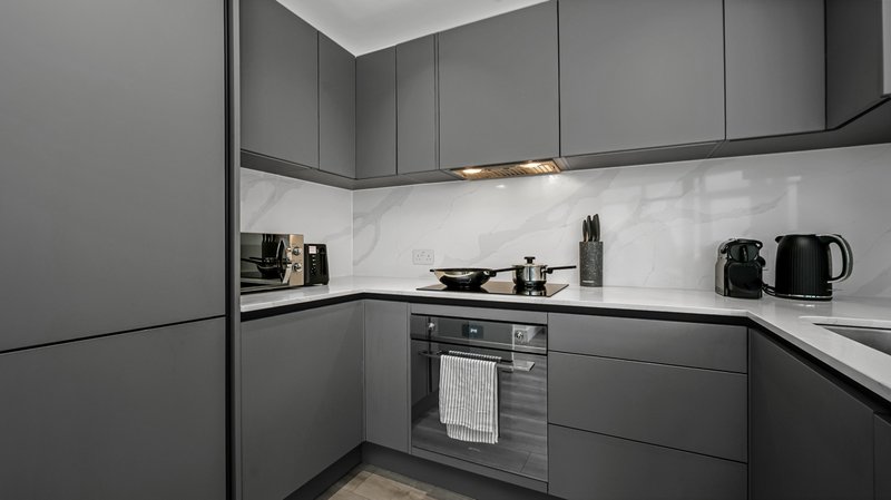 Modern kitchen with dark grey cabinets, white splashback, built-in oven and counter appliances