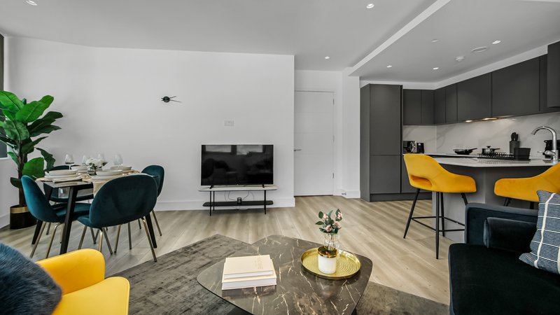 Modern open-plan living and kitchen area with yellow chairs, dark cabinetry, and wooden flooring