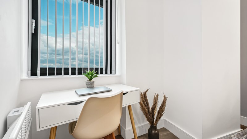 Compact home office with desk, chair, small plant, and window with sky view