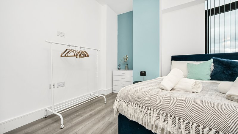 Modern bedroom with double bed, teal accent wall, white furniture and pendant lamp