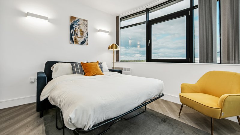 Modern bedroom with double bed, yellow armchair, large window with city view