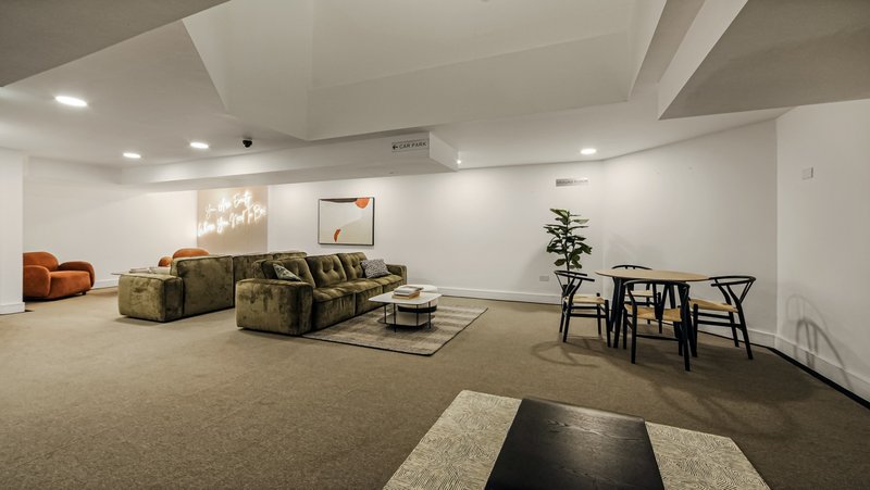 Open-plan basement lounge with modular sofa, dining table, orange armchair and potted plant
