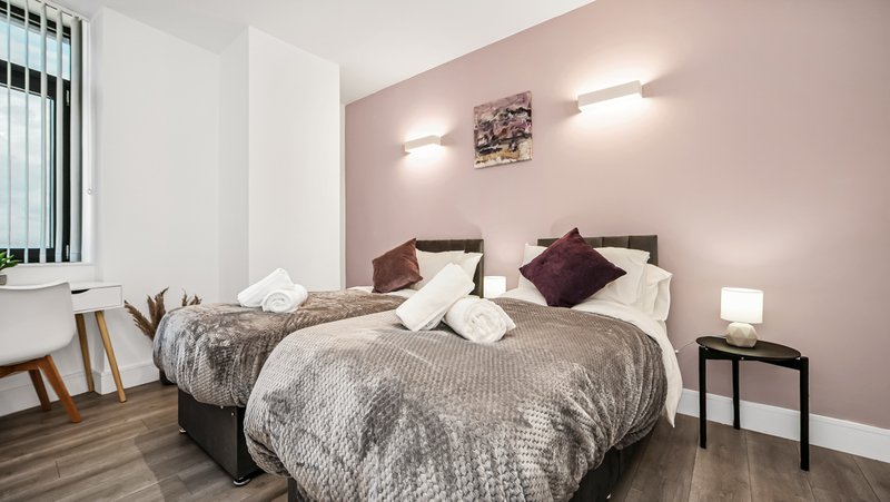 Modern bedroom with two beds, pink walls, wooden flooring and bedside lamp