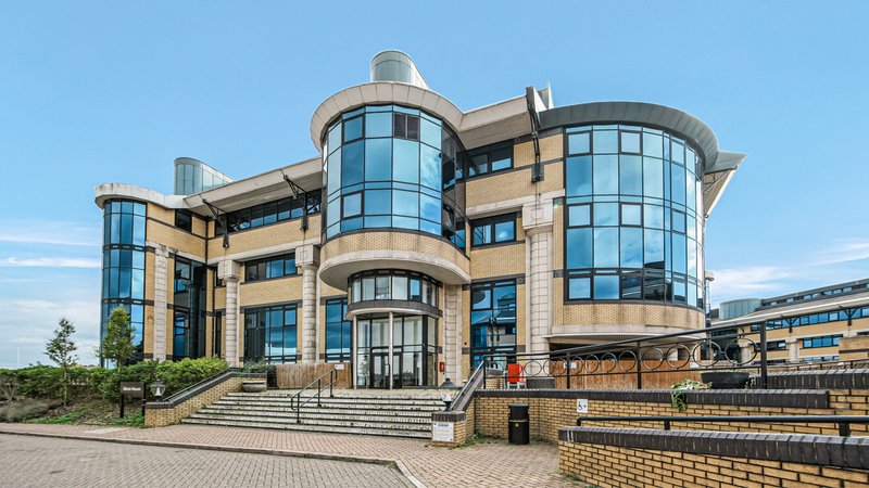Modern curved stone and glass building exterior with entrance steps and courtyard paving