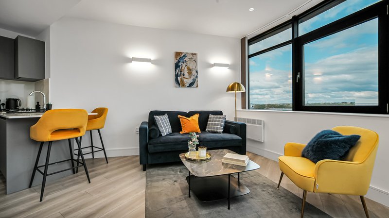 Modern open-plan living room with yellow accent chairs, black sofa, and large windows with city view