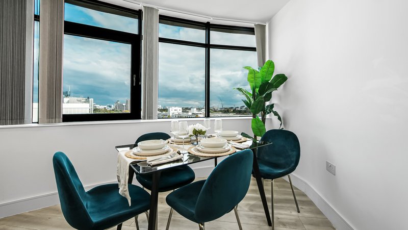 Modern dining area with table, teal chairs, large windows overlooking cityscape and plant