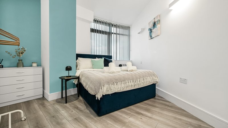 Modern bedroom with double bed, turquoise accent wall, white dresser, and vertical blinds