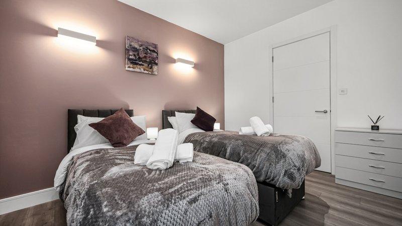 Modern bedroom with two beds, mauve accent wall, white bedding and dark pillows