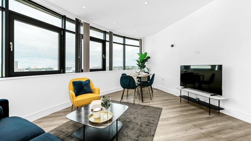Modern living room with yellow armchair, TV, large windows overlooking cityscape