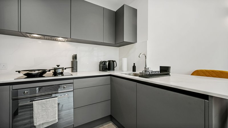 Modern grey kitchen with built-in oven, white countertop and breakfast bar seating