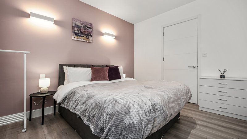 Modern bedroom with queen bed, mauve walls, white wardrobe and bedside lighting