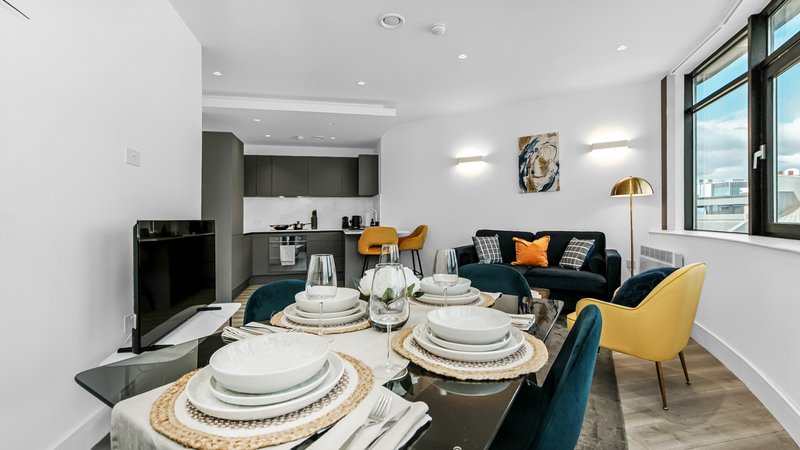 Open-plan dining and living area with set table, kitchen, sofa and large windows