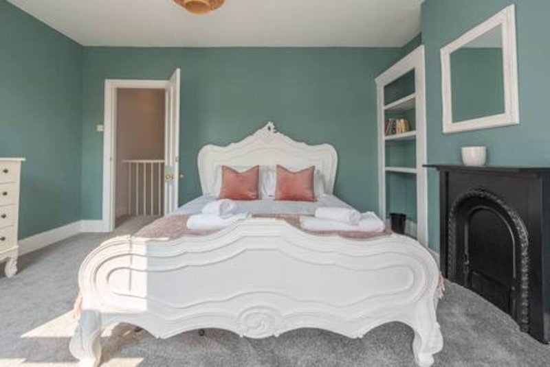 Bedroom with ornate white bed, teal walls, fireplace, and built-in shelving