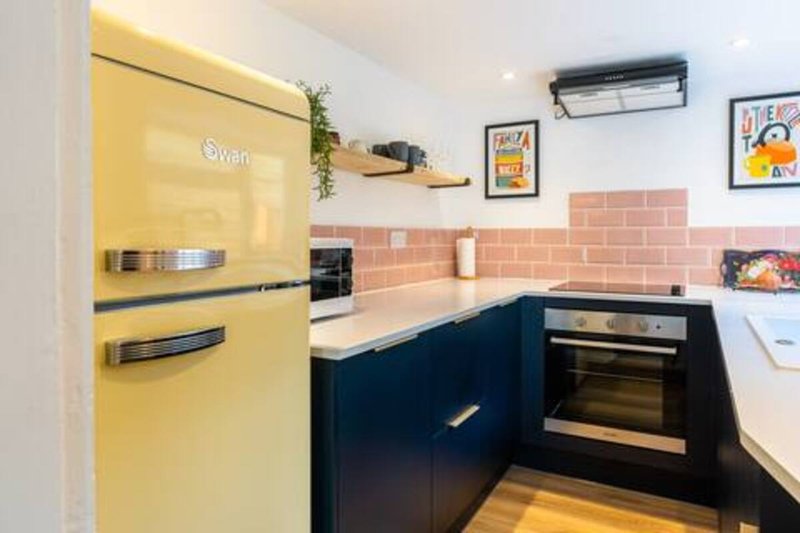 Modern kitchen with yellow retro fridge, black cabinetry, pink tile backsplash and wall art