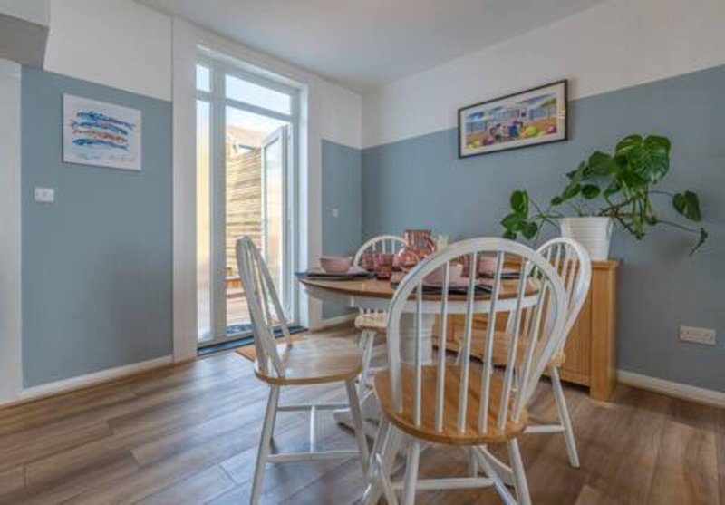 Dining area with wooden table, white chairs, potted plant and glass doors to garden