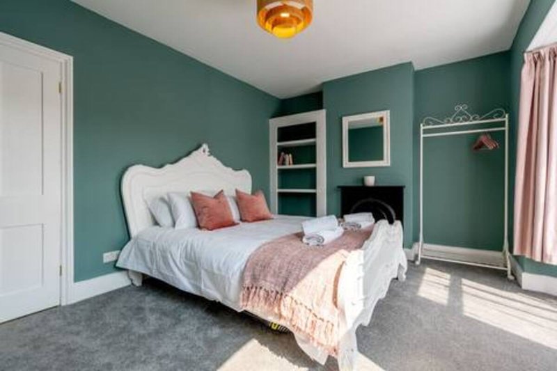 Bedroom with ornate white bed, teal walls, built-in shelving, and gold ceiling light