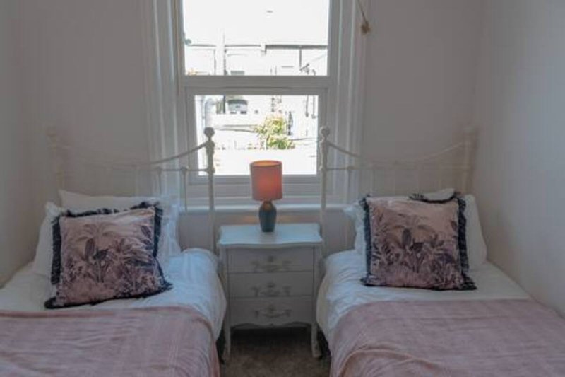 Twin bedroom with two single beds, decorative pillows, bedside table and window with street view