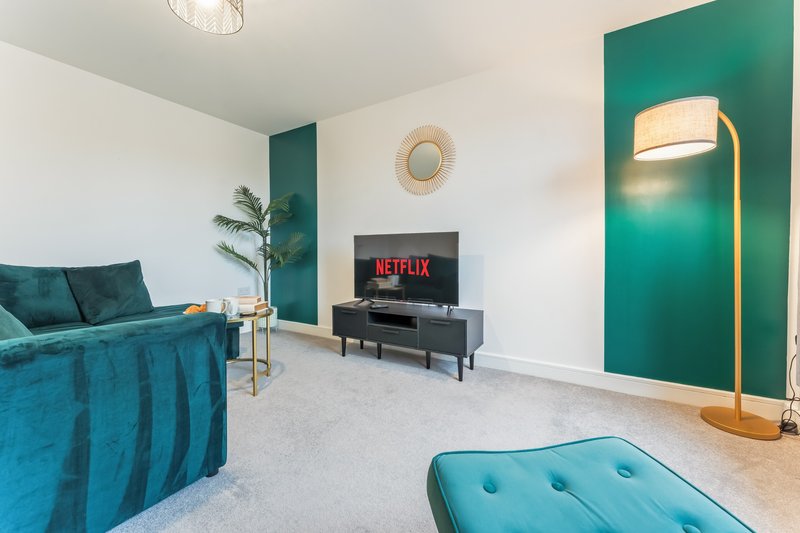 Modern living room with teal sofa, TV entertainment unit, ottoman, and accent wall