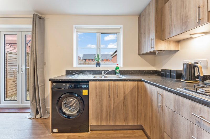 Modern kitchen with wooden cabinets, black countertop, washing machine and window view