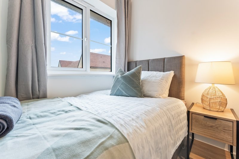 Bright bedroom with single bed, grey headboard, bedside lamp and window with street view