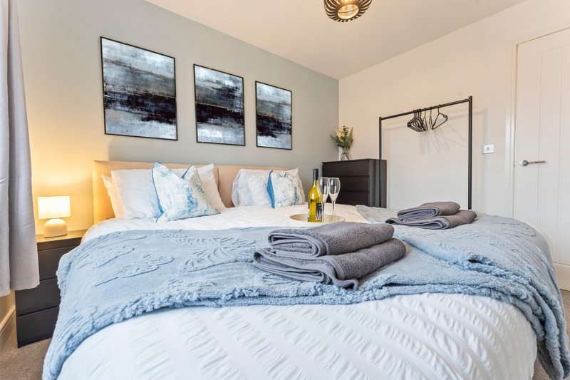 Modern bedroom with double bed, blue bedding, rolled towels, framed wall art and bedside lamp