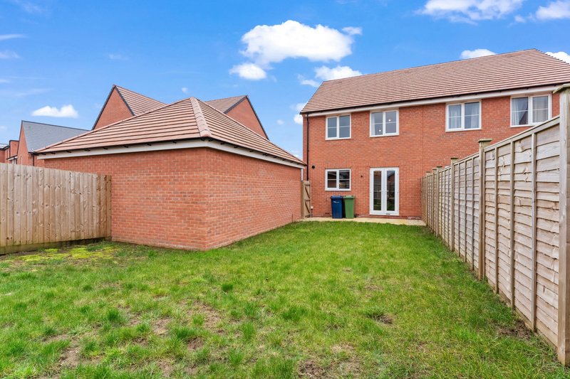 Rear garden view of brick detached house with lawn, wooden fencing and clear sky