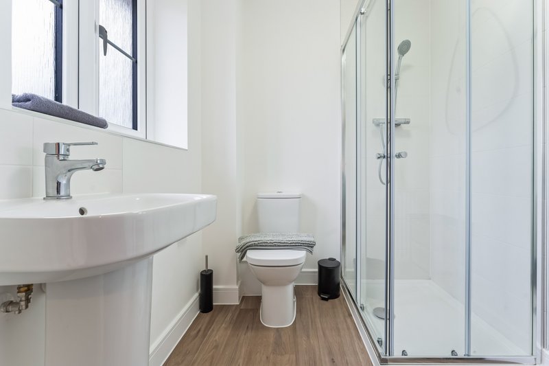 Modern bathroom with curved white sink, toilet, and glass-enclosed shower cubicle
