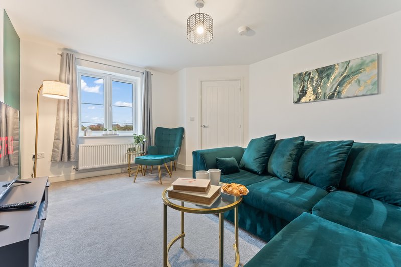 Bright modern living room with teal corner sofa, armchair, coffee table and windows overlooking landscape