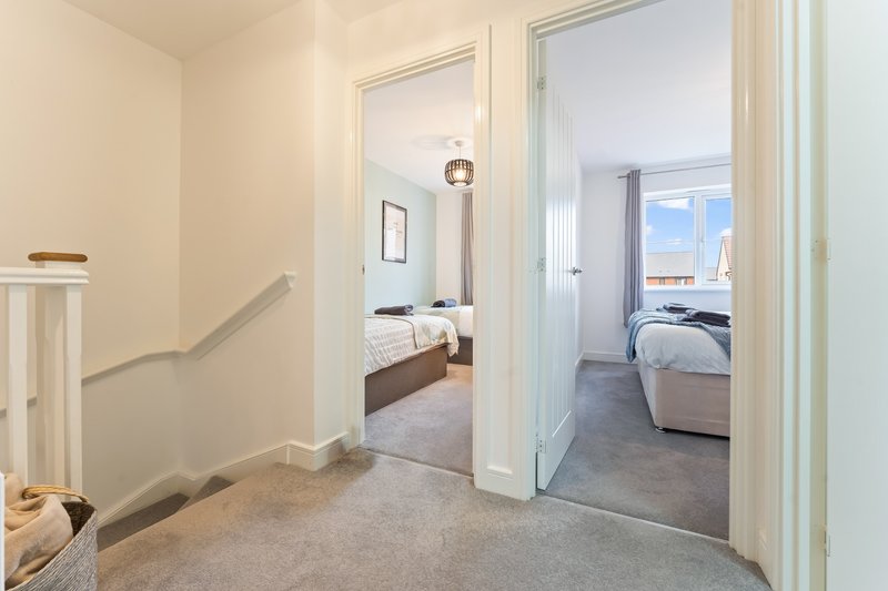 Hallway with staircase leading to two bedrooms with open doors showing beds