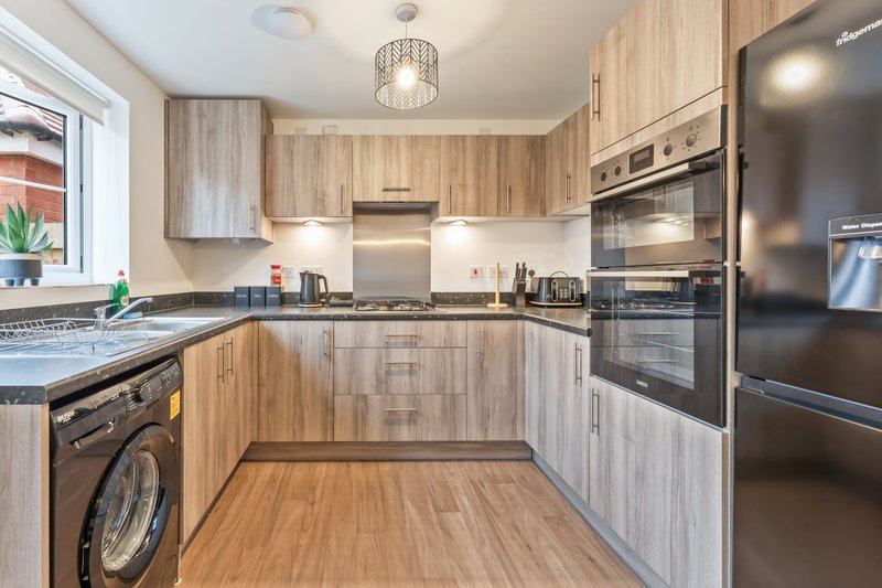 Modern kitchen with light wood cabinetry, stainless steel appliances, and wooden flooring