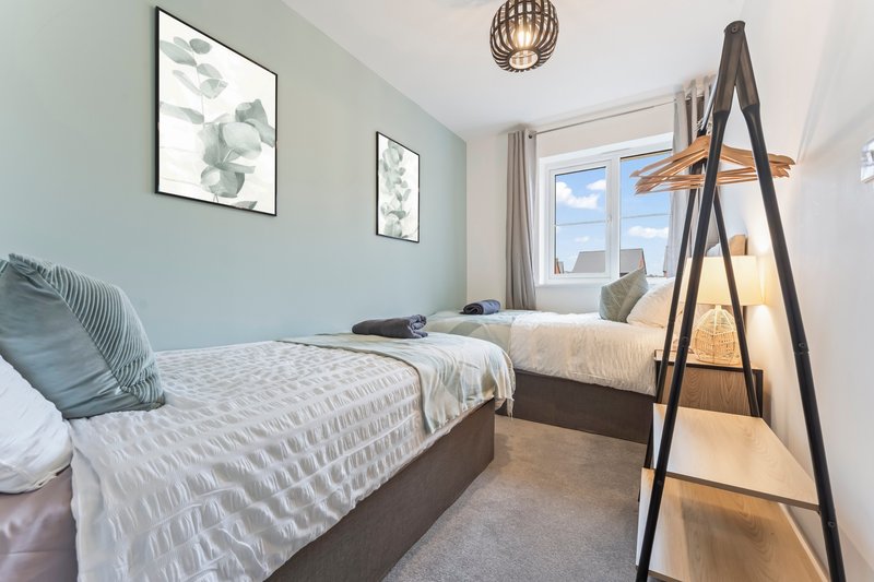 Bright bedroom with two single beds, botanical wall art, ladder shelf, and window with sea view